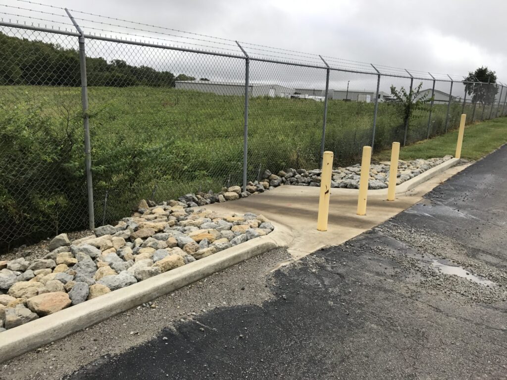 Stormwater discharge outlet with bollards, curbing, and riprap erosion control, illustrating best management practices for NPDES No Exposure Certification.