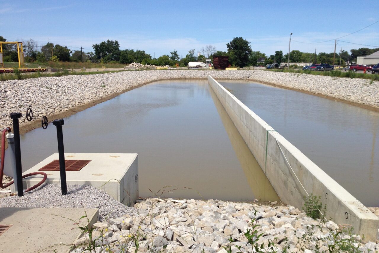 Engineered stormwater retention pond with flow separator at a steel manufacturing facility, designed to improve drainage and reduce TSS in compliance with NPDES requirements.