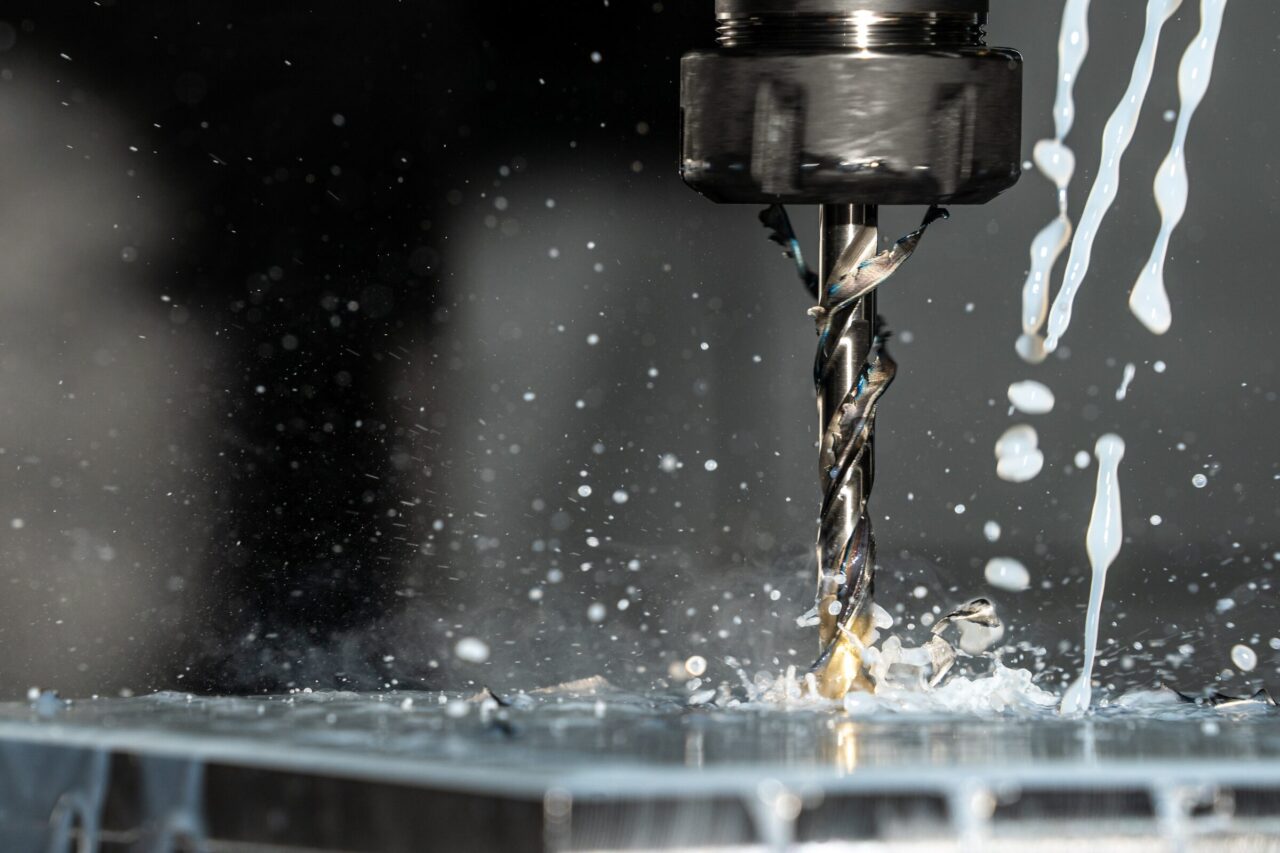 Close-up of industrial metal drilling with coolant spray, symbolizing multi-year EHS compliance audits in manufacturing environments.