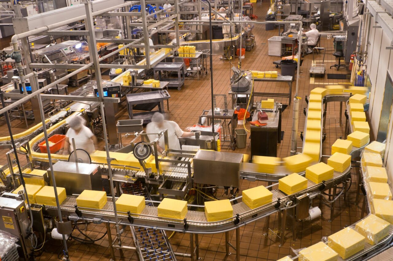 Cheese processing facility with conveyor belts and staff, illustrating industrial food manufacturing operations audited for environmental compliance.