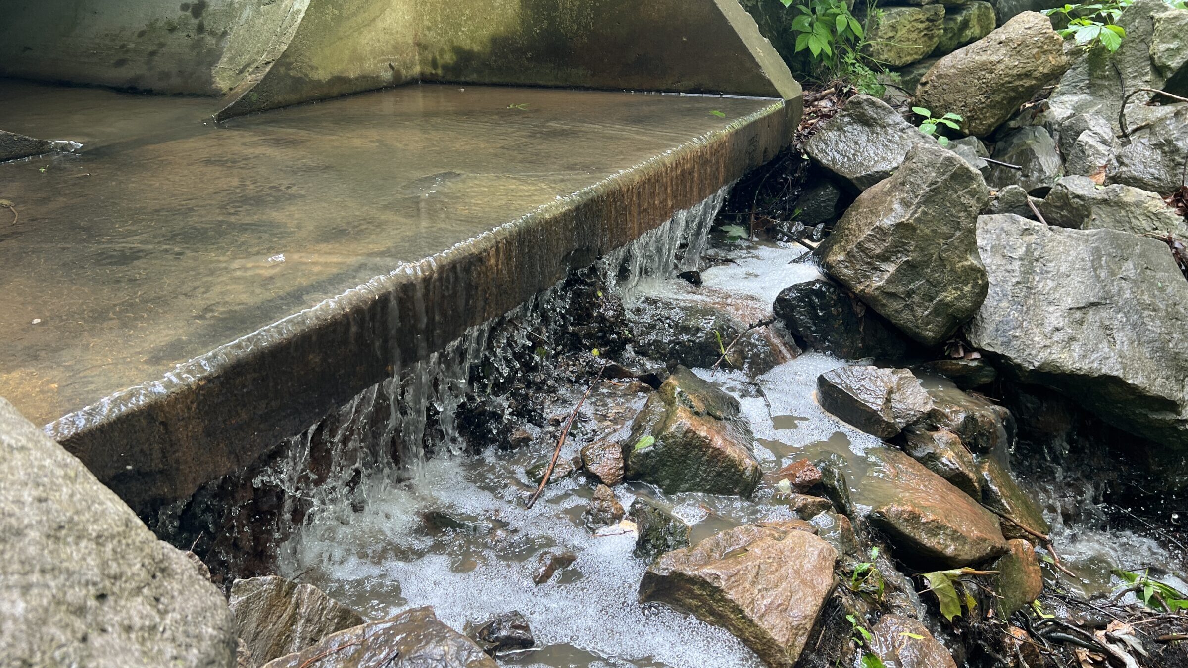Stormwater runoff flowing from a concrete culvert over rocks, illustrating discharge conditions relevant to No Exposure Certification for NPDES stormwater permit exclusion.